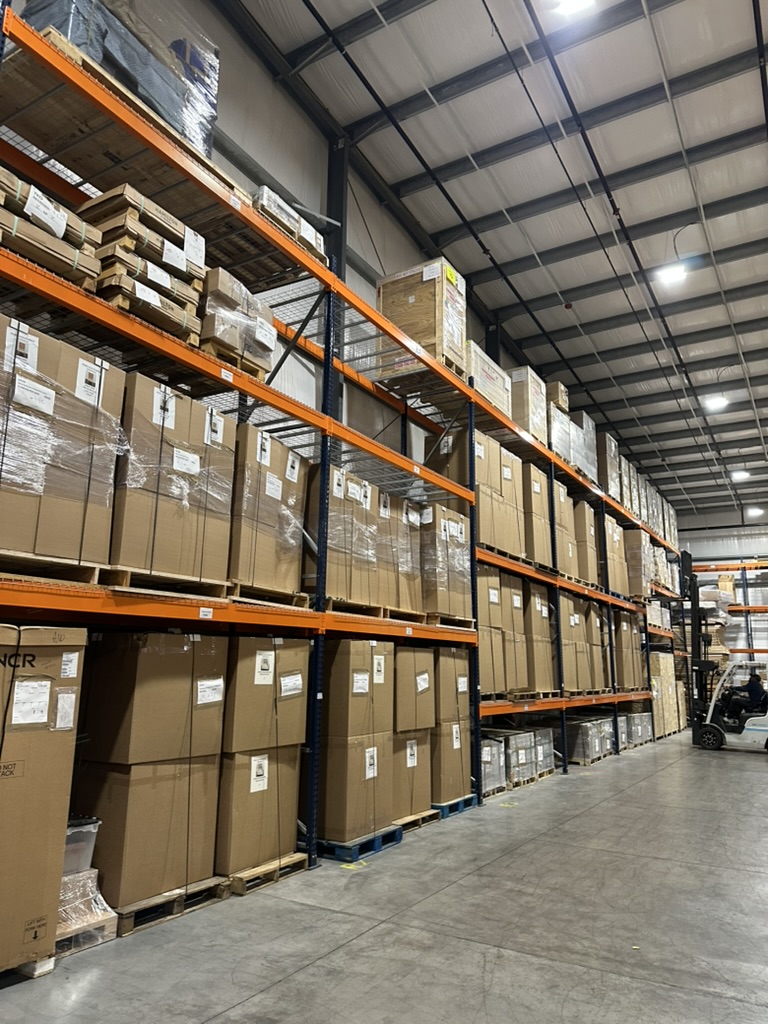 Shelves in a warehouse full of boxes, with a forklift in the background